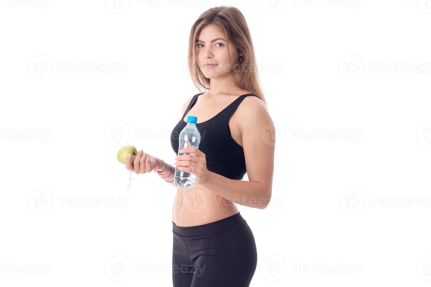 slim girl in a black top and tights stands sideways  holds in one hand apple  water photo