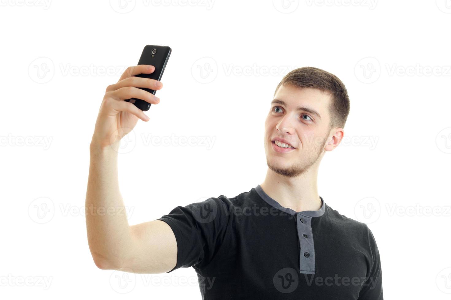 a close-up portrait of young smiling guy in a t-shirt that makes photo on phone