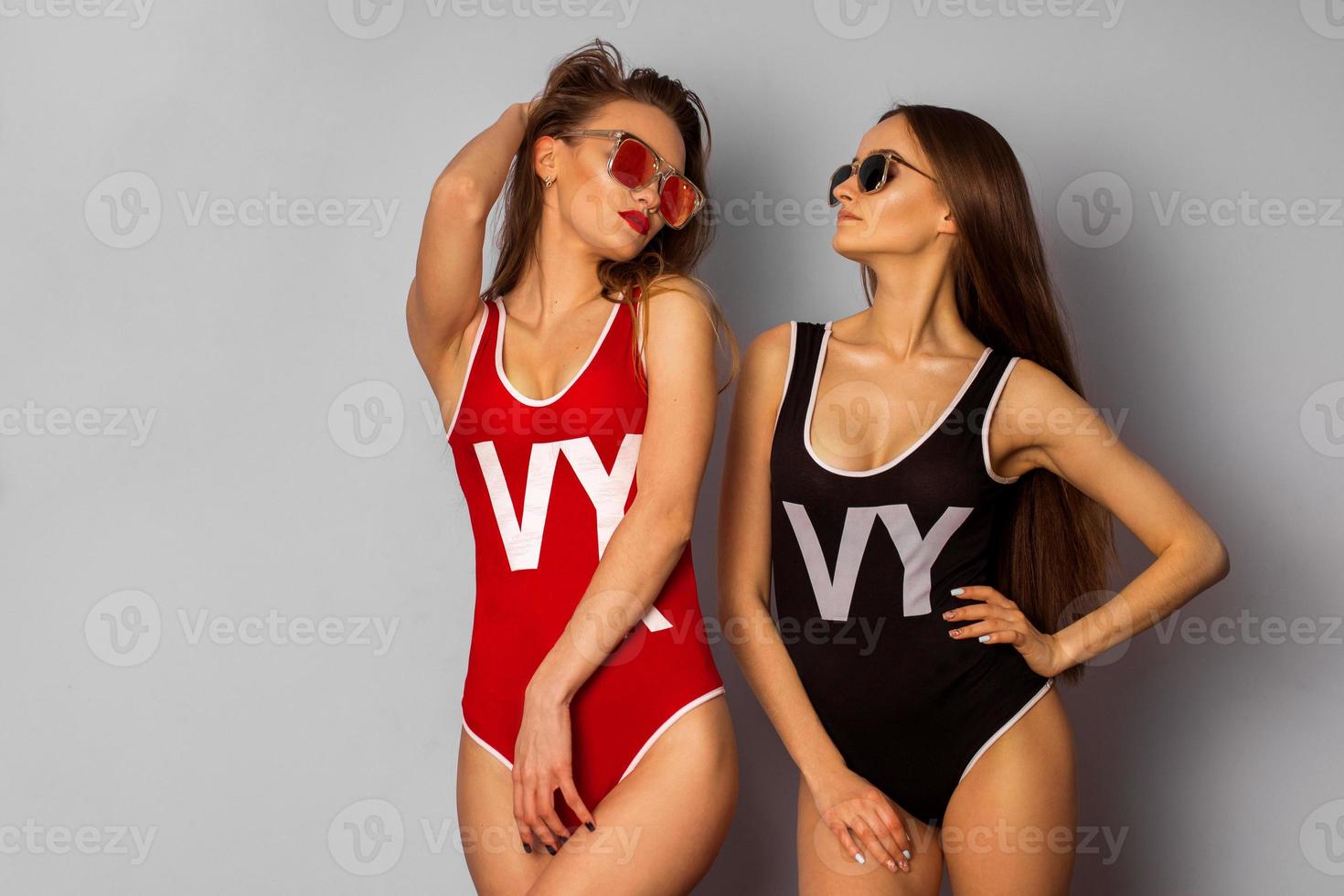 two young sexy girls in body swimsuit and sunglasses in studio photo