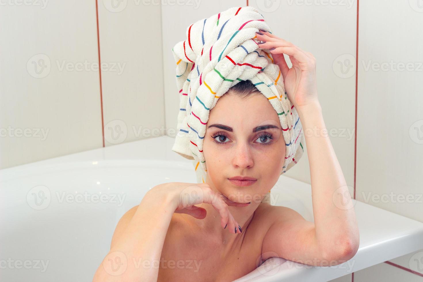beautiful young girl with towel on the hair lies in the bathroom and looks straight photo