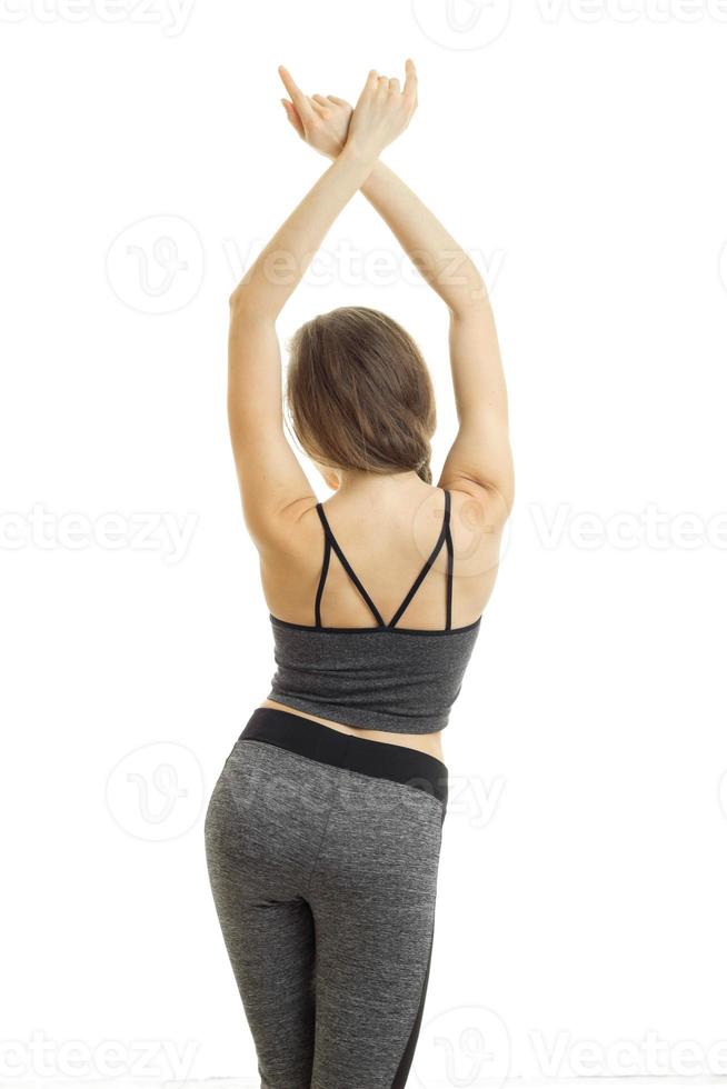 athletic young girl in grey trousers and top worth turning your back to the camera holding up hands up photo