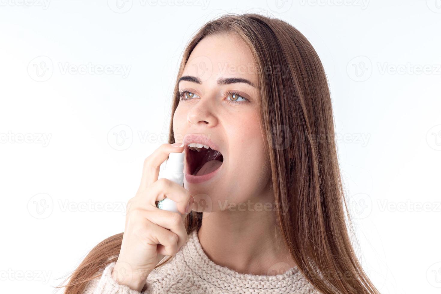 una joven que echa chorros de spray para el dolor de garganta está aislada en un fondo blanco foto