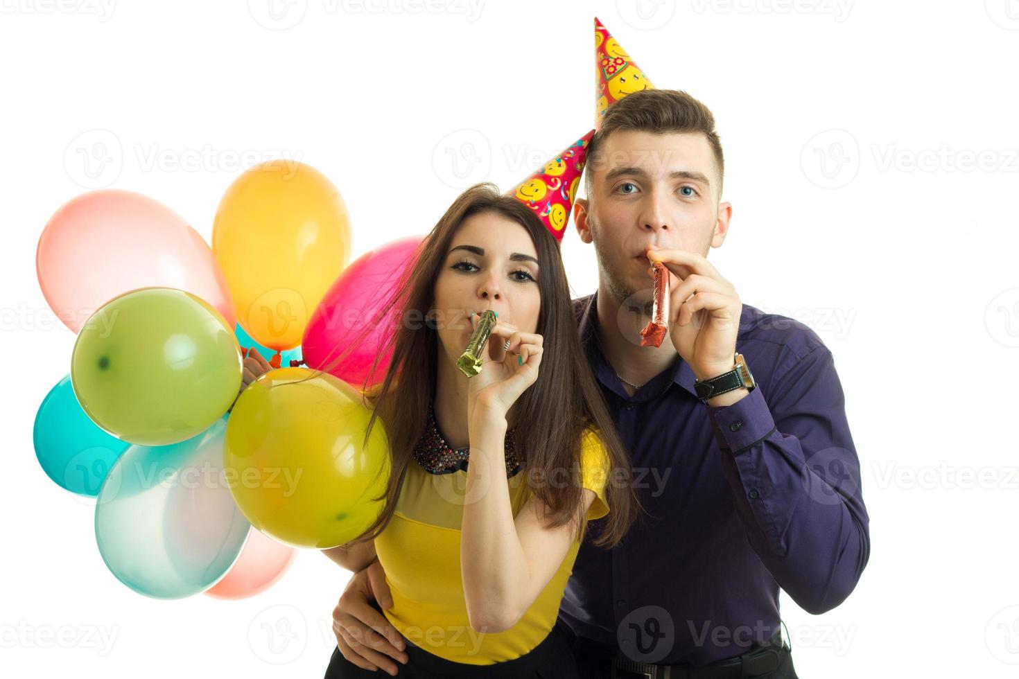 un chico y una chica hermosos y felices esperan soplar cuernos y llevar muchas bolas de colores foto