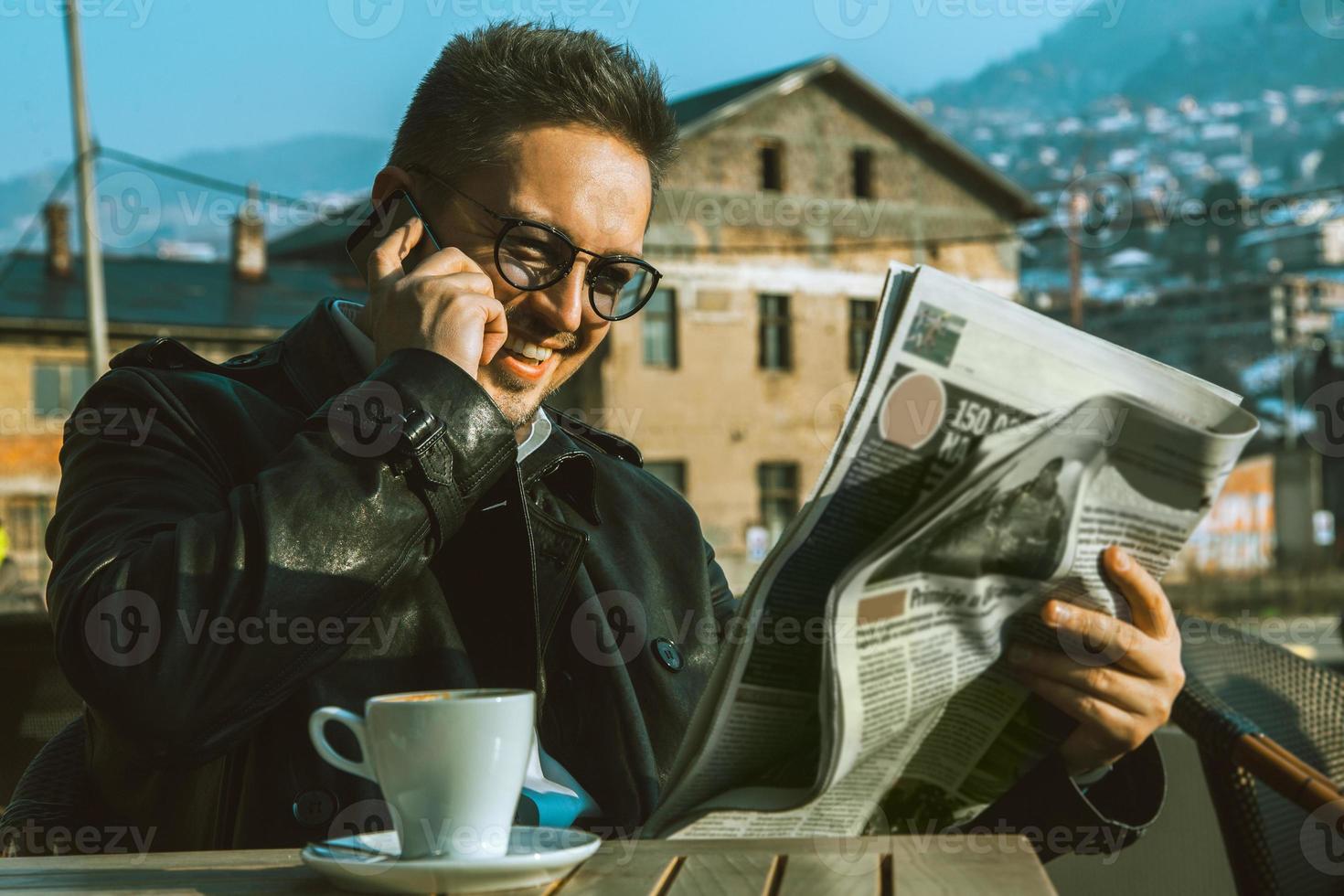 hombre adulto divertido leer el periódico hablando por teléfono y tomando café foto