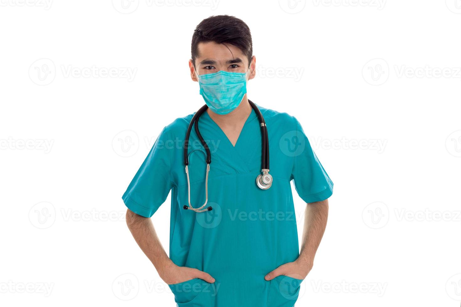 young male doctor in uniform and mask with stathoscope posing isolated on white background photo