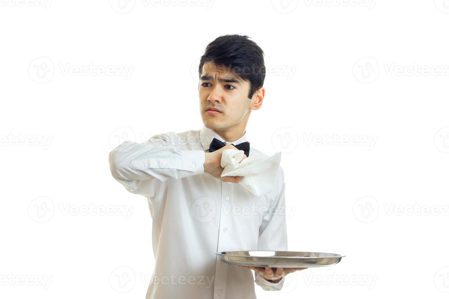 serious young waiter in a shirt holding a towel in the other hand holds the tray and looks toward photo