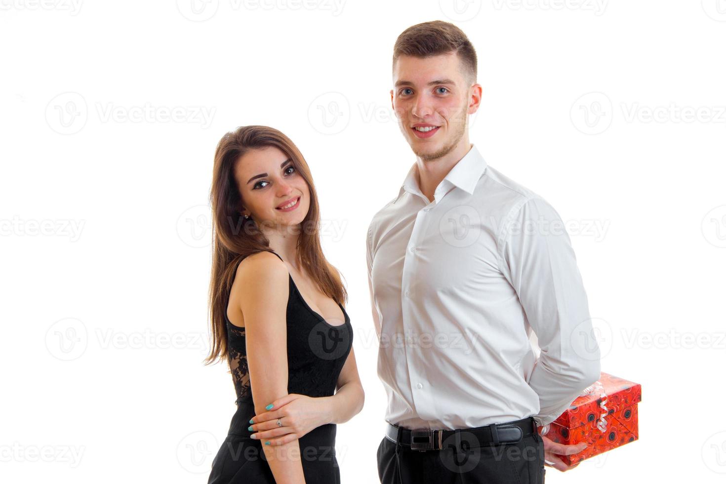 charming young girl smiles and stands near the guy in the white shirt that keeps behind gift photo