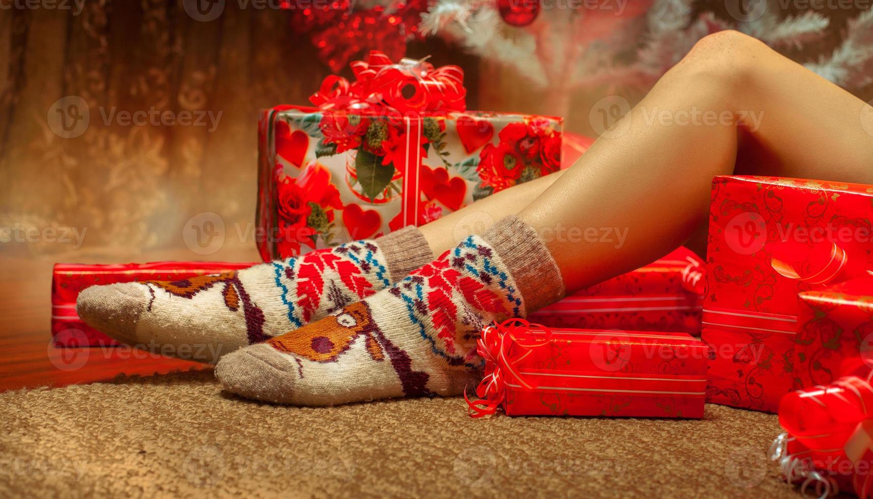 Horizontal photo of sexy female legs in funny socks with a lot of christmas gifts