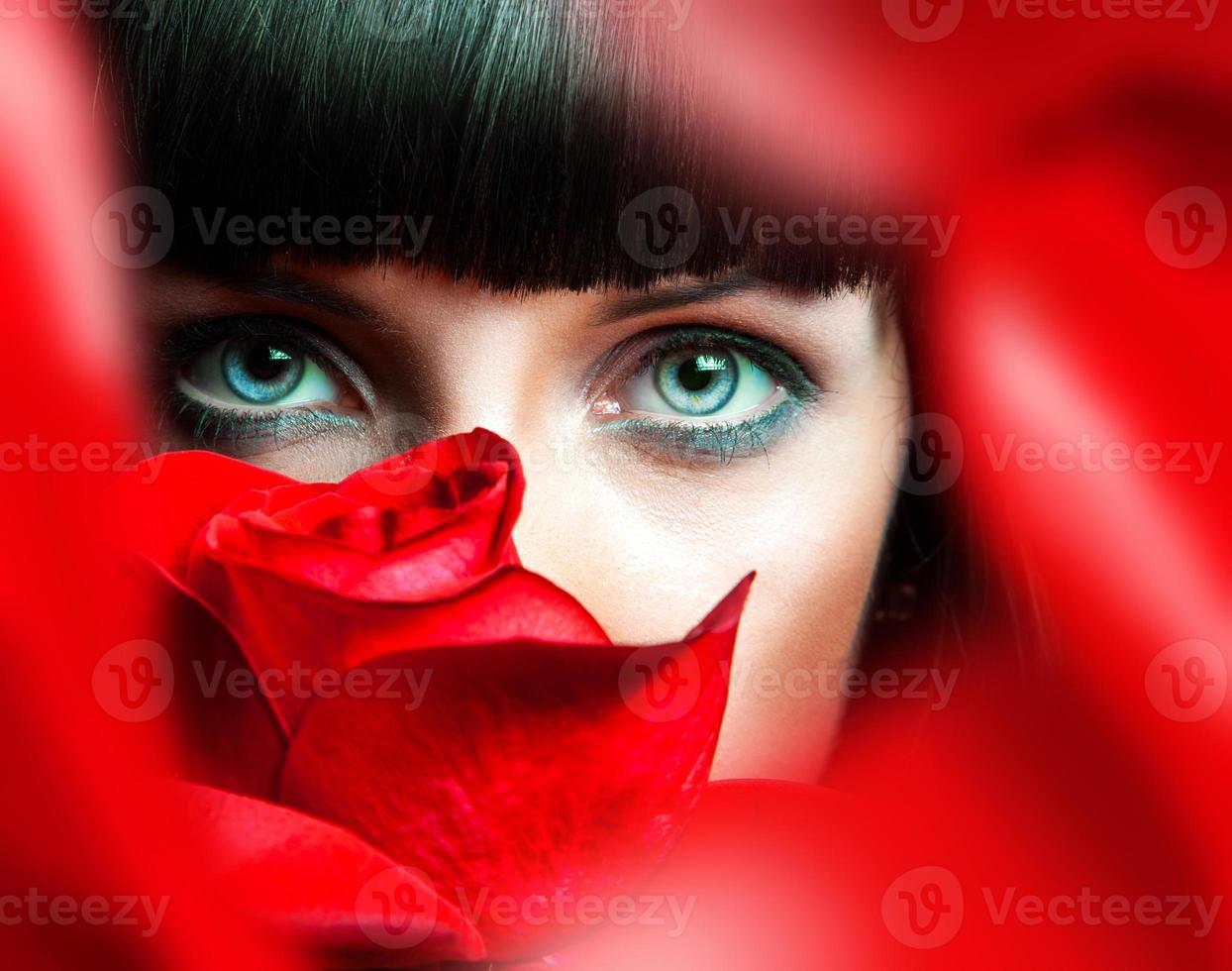 Preciosa morena detrás de una rosa roja en el estudio foto