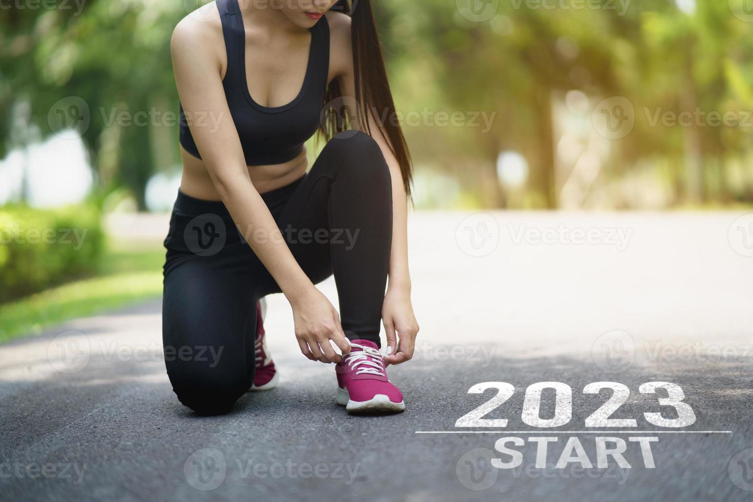 Sport woman runner tie shoelaces start into the new year 2023. Start up of runner woman running on nature race track go to Goal of Success. People running as part of Number 2023. Sport health care. photo