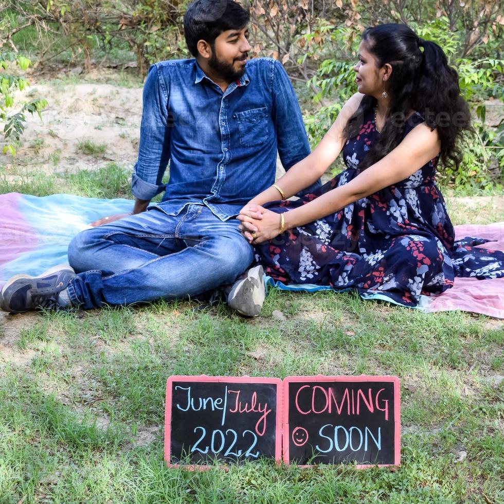 Indian couple posing for maternity baby shoot. The couple is posing in a lawn with green grass and the woman is falunting her baby bump in Lodhi Garden in New Delhi, India photo