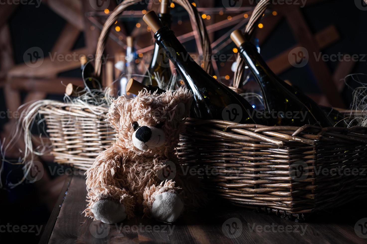 Teddy bear, champagne bottle with Christmas basket, gold garlands on dark brown wooden background, new year celebration concept photo