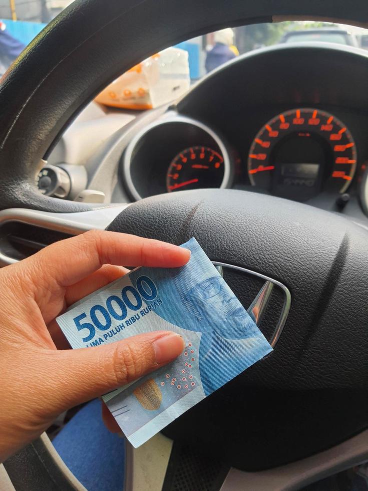 Jakarta, Indonesia on July 2022. A hand is holding a fifty thousand rupiah bill which bends while driving. photo