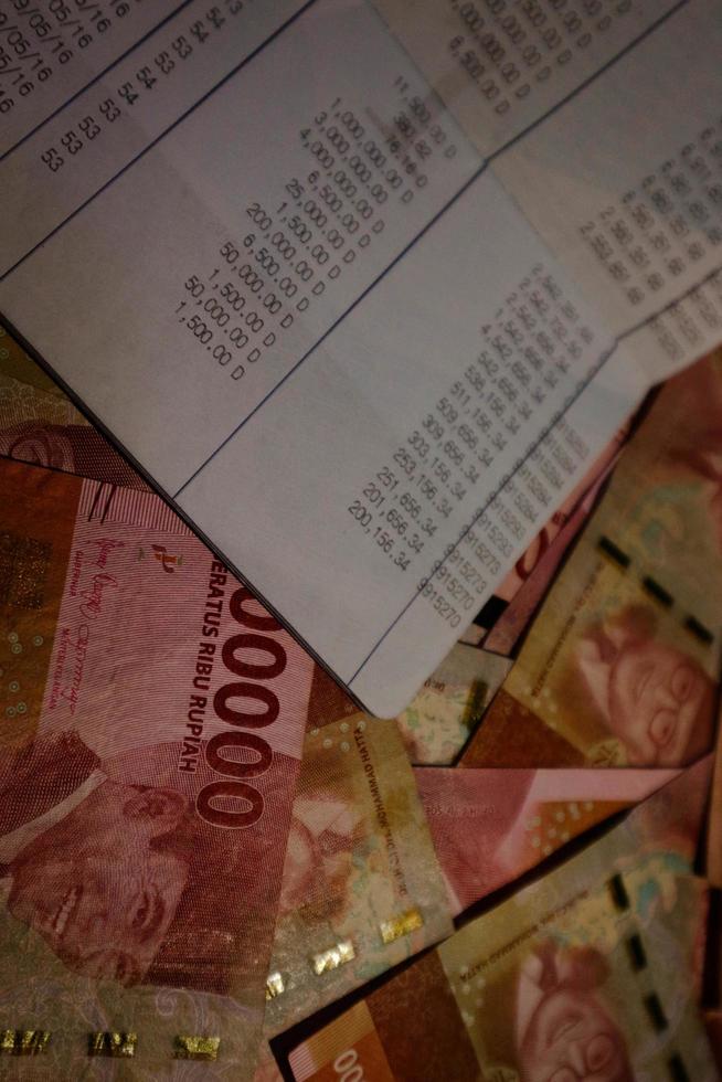 Jakarta, Indonesia on July 2022. A savings book on top of several hundred thousand rupiah bills scattered around. photo