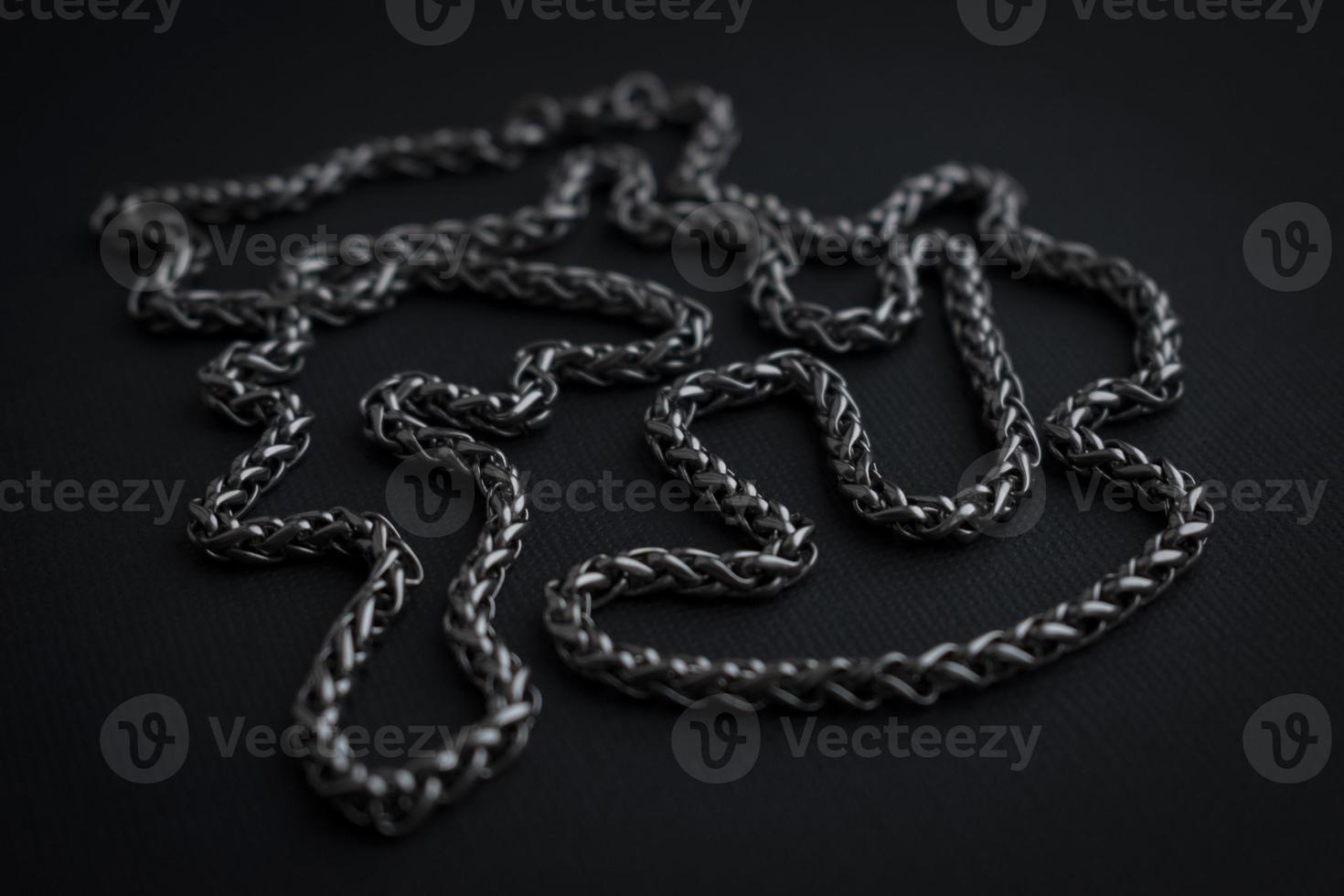 Metallic necklace on black background. Silver color chain. Dark cold color photo. Men's necklace. Thick chain. Male necklace. Stainless jewelry. Necklace detail. photo