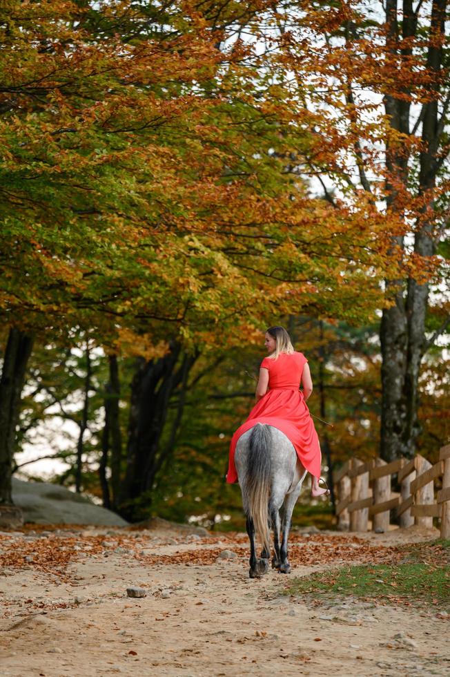 A woman in a red dress sits on a horse, an autumn walk in the forest. photo