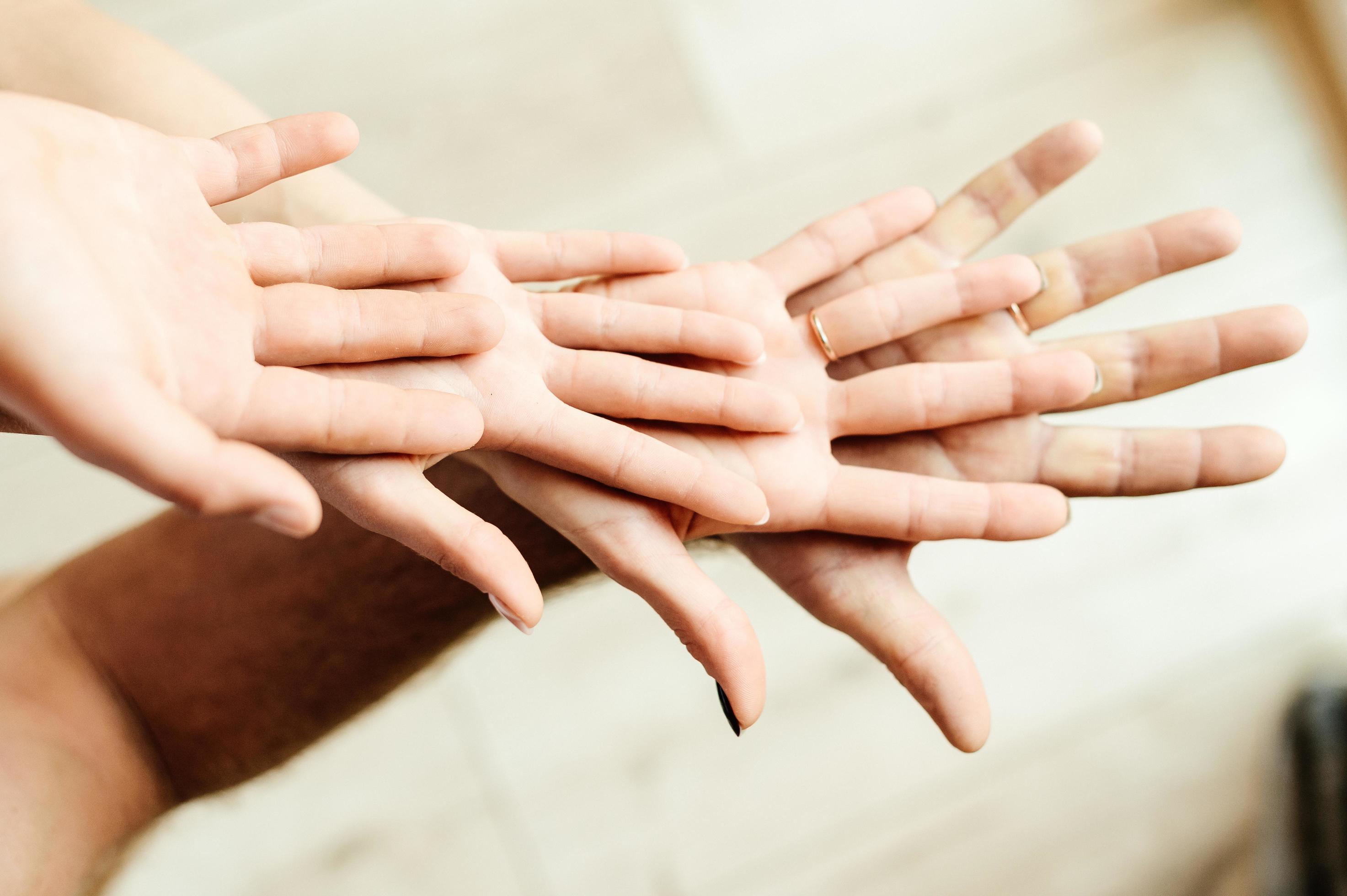 Four hands placed on top of each other palms up, unity of parents