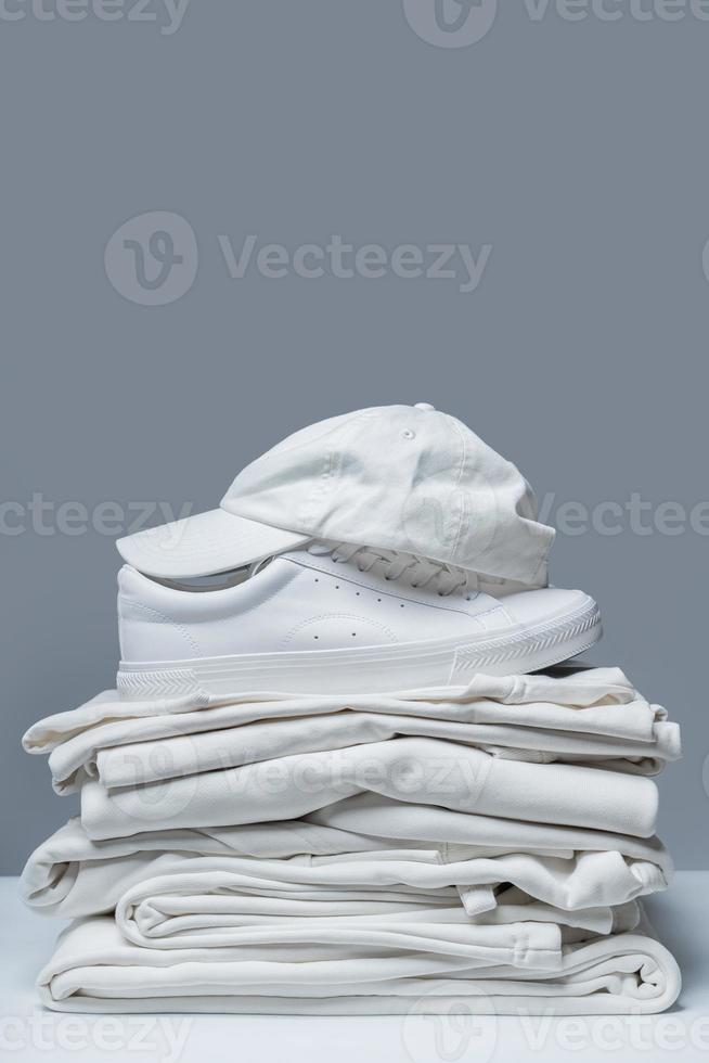 Stack of white clothes, trainers and baseball cap photo