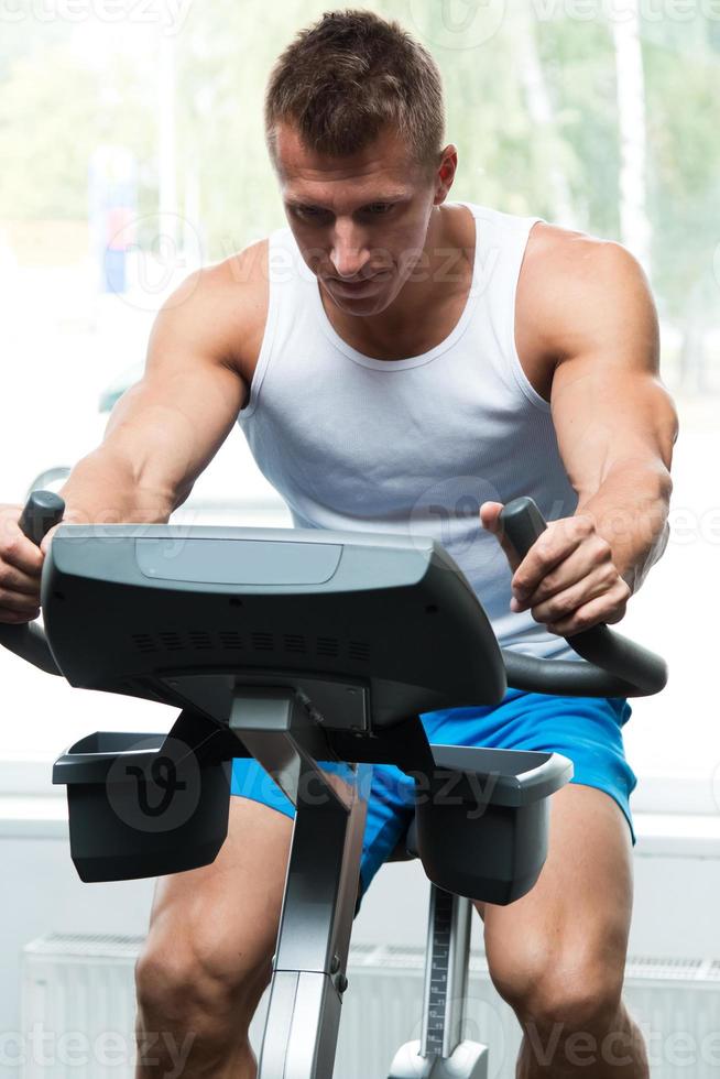 joven musculoso en bicicleta estática en el gimnasio foto