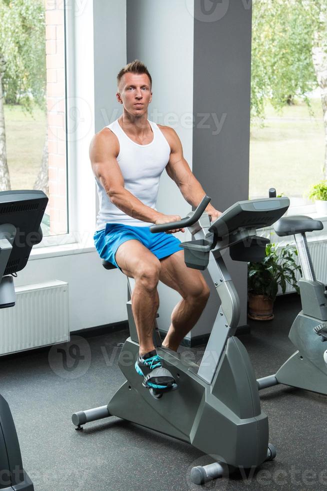 joven musculoso en bicicleta estática en el gimnasio foto