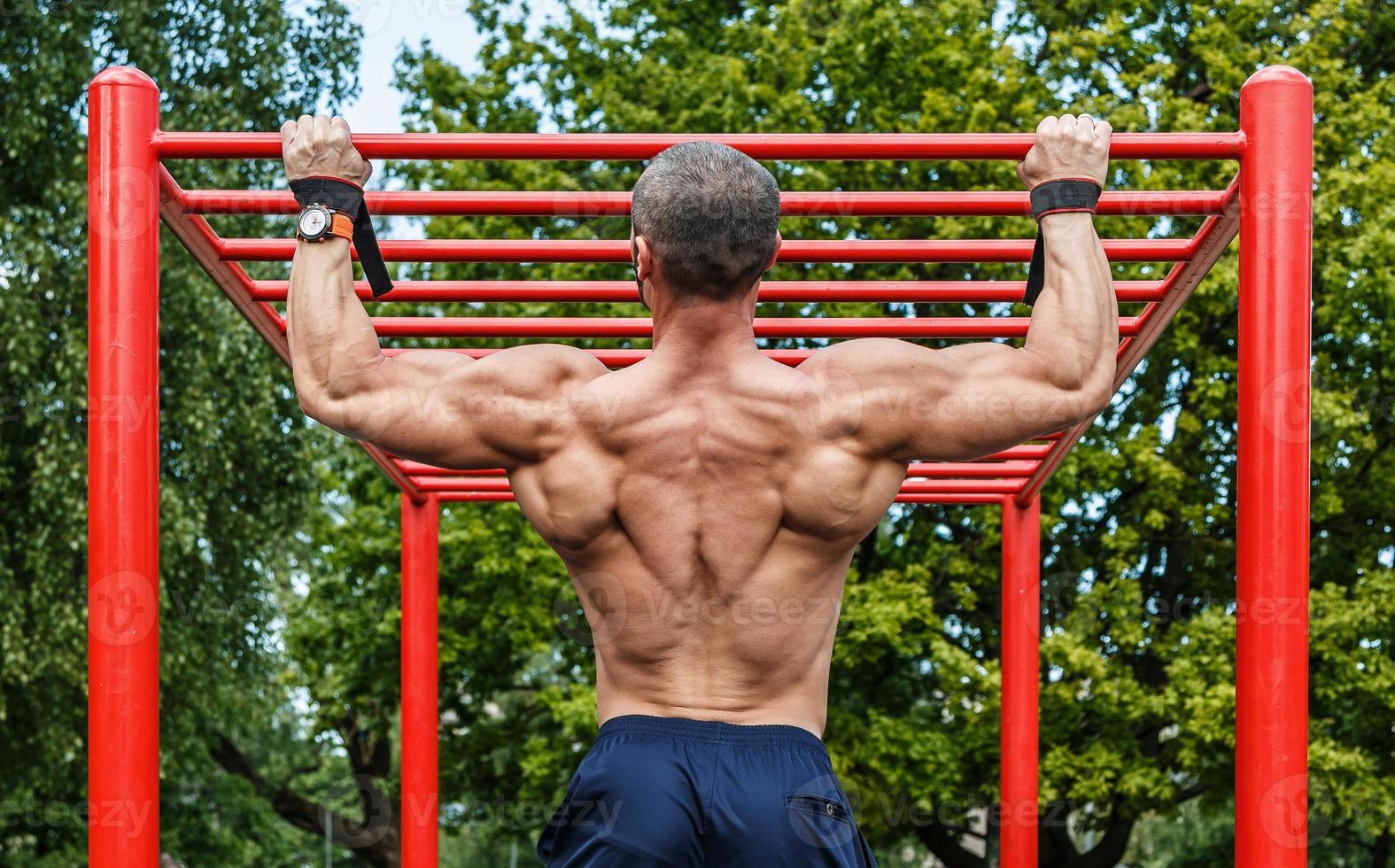 Muscular man doing pull-ups on horizontal bar photo