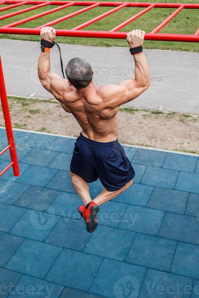 Muscular man doing pull-ups on horizontal bar photo