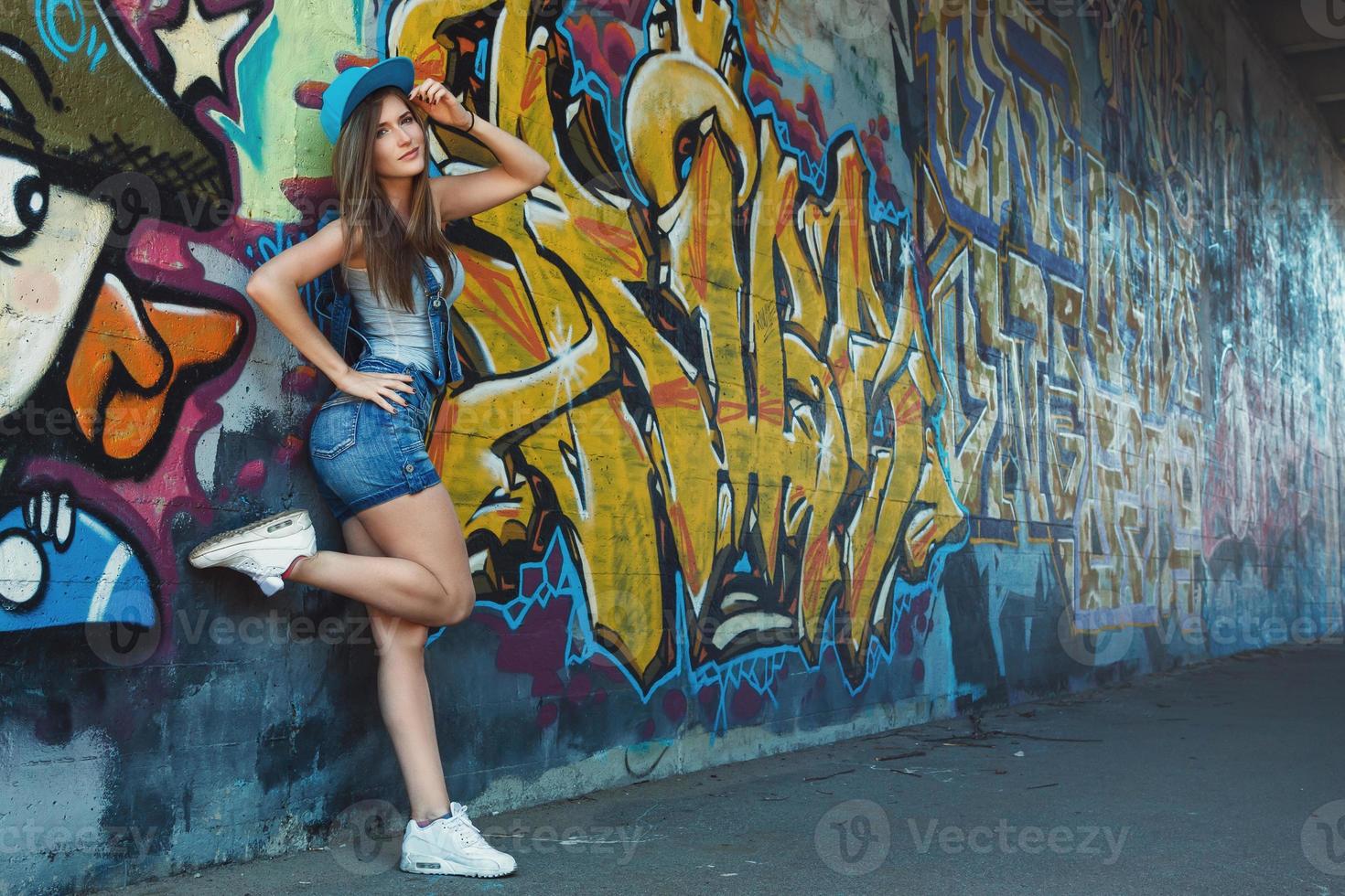 chica en overoles de mezclilla posando contra la pared con graffiti foto