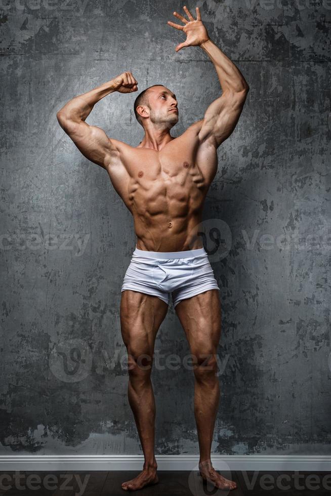 Sexy and muscular man posing against concrete wall photo