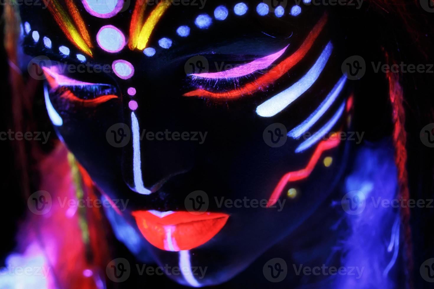Woman in image of Native American with neon makeup, which made of fluorescent paint in ultraviolet light. photo