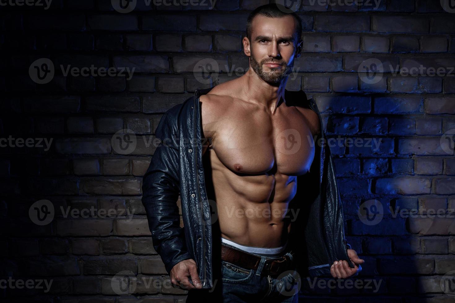 Muscular man in leather jacket against brick wall photo