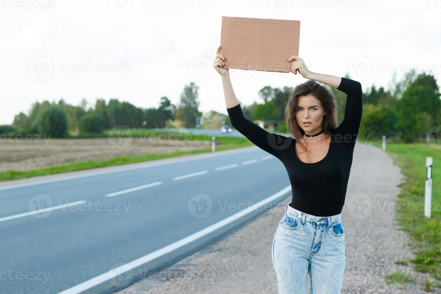 autostopista en la carretera tiene un cartel de cartón en blanco foto