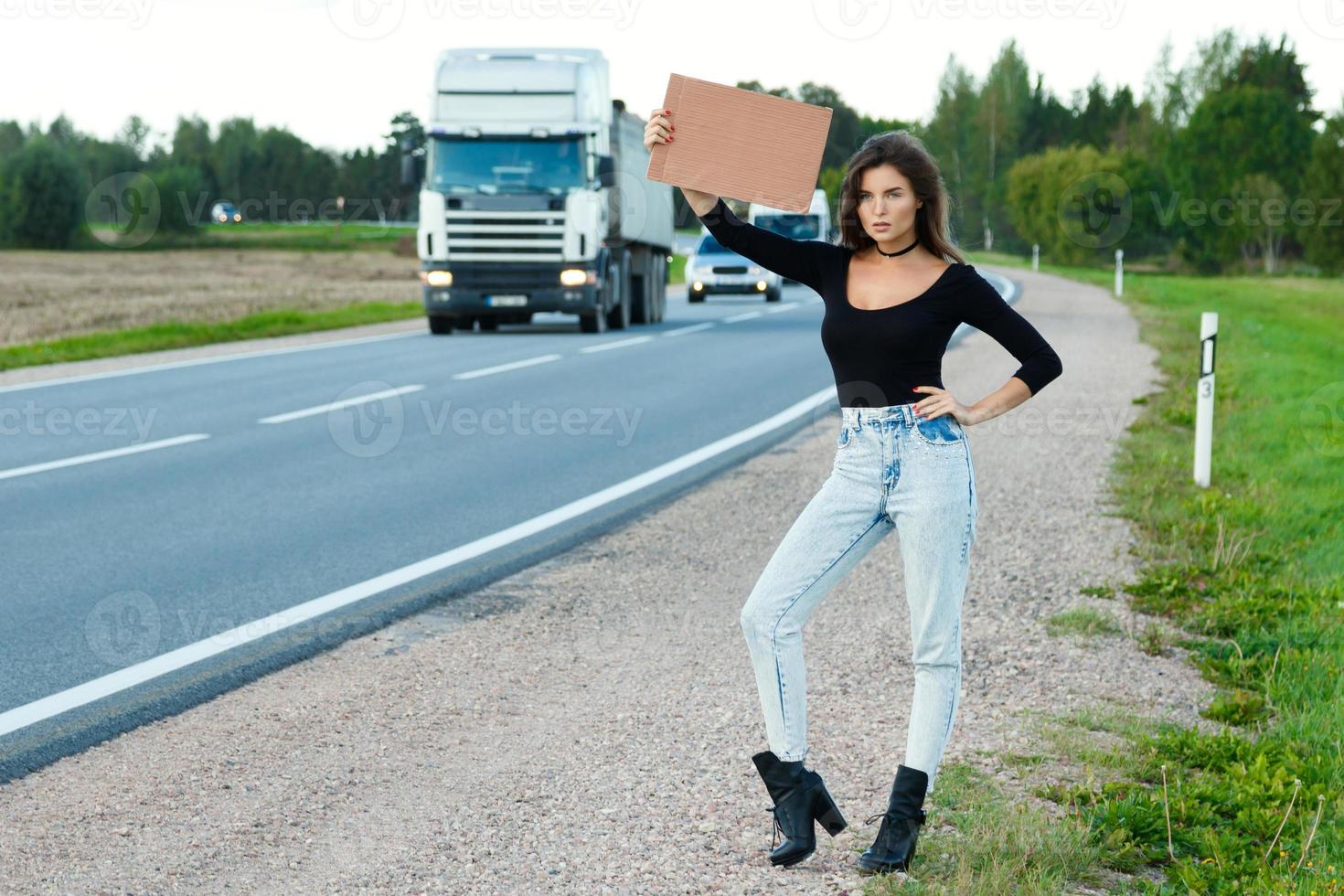 Hitchhiker on the road is holding a blank cardboard sign photo