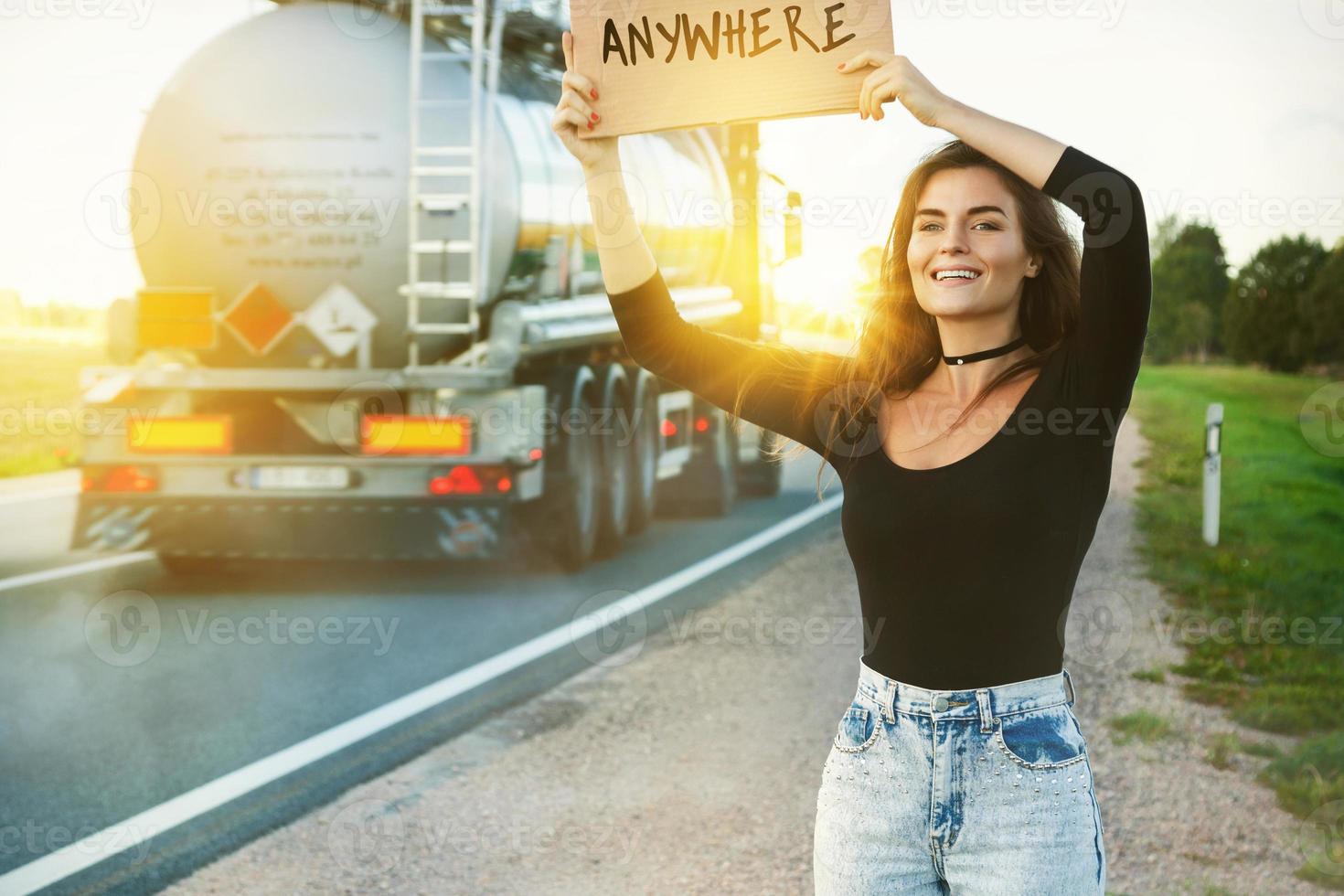 Woman on the road is holding cardboard sign with word ANYWHERE photo