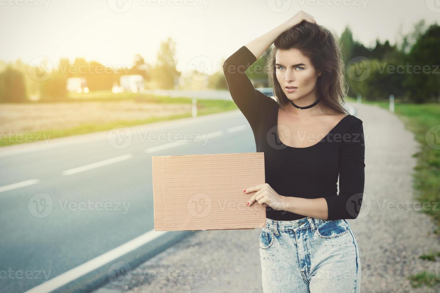 Hitchhiker on the road is holding a blank cardboard sign photo