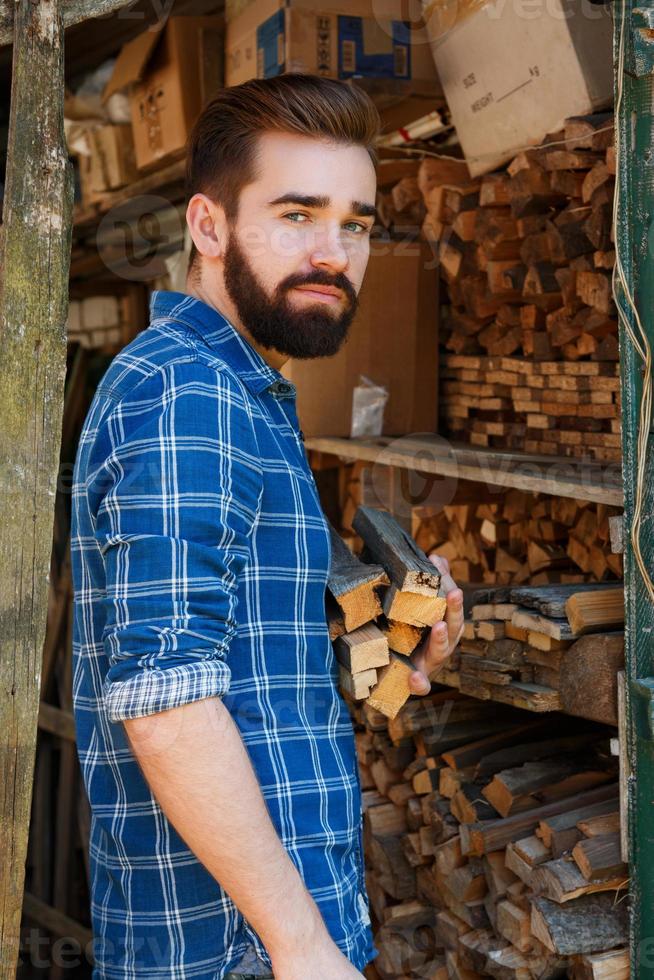 Handsome bearded man with firewoods in village photo