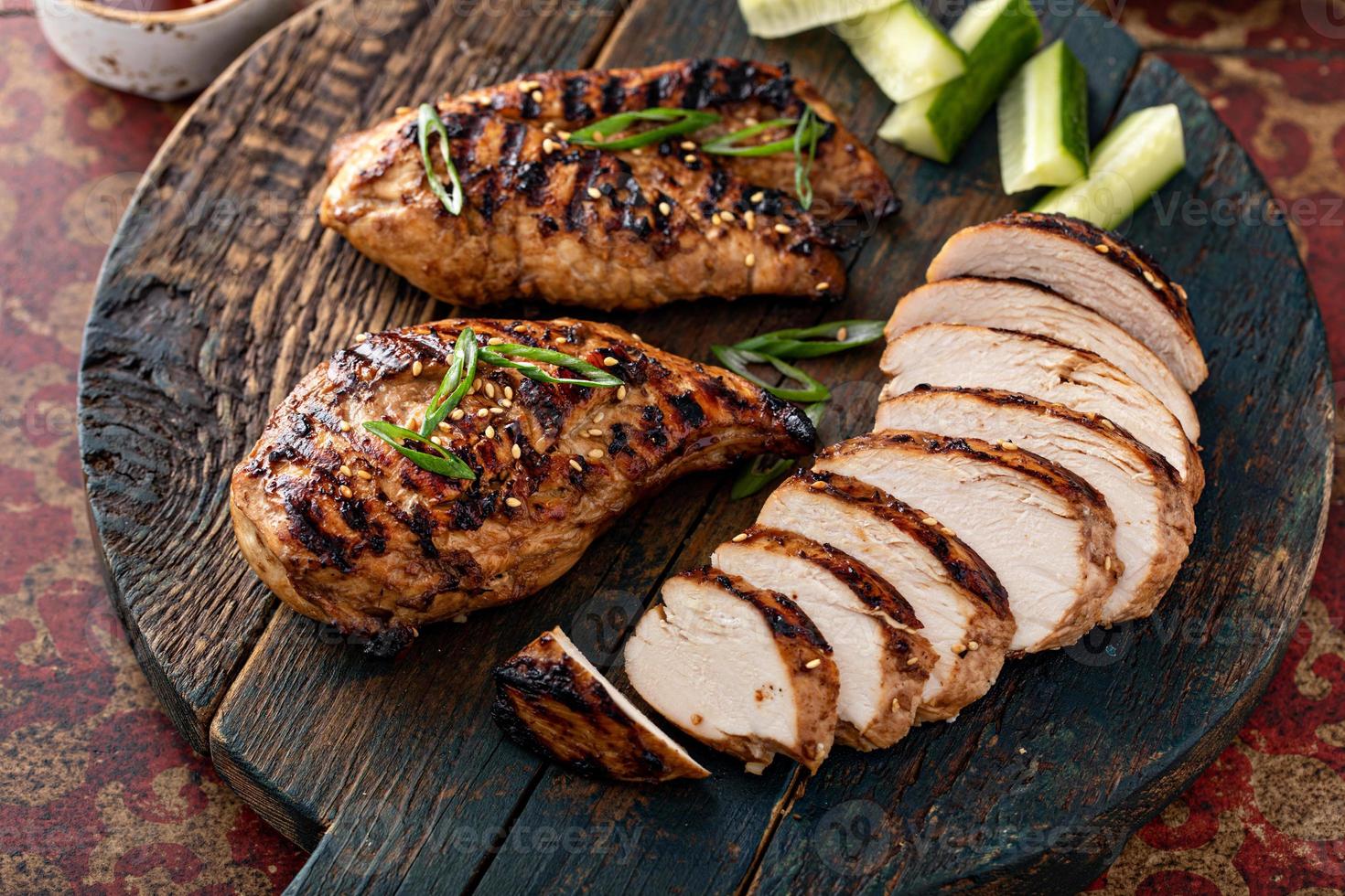 Grilled teriyaki chicken breast sliced on a board with green onions photo