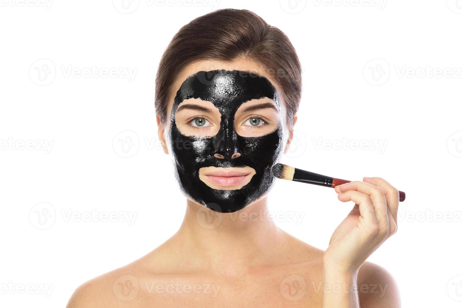 Beautiful woman is applying purifying black mask on her face photo