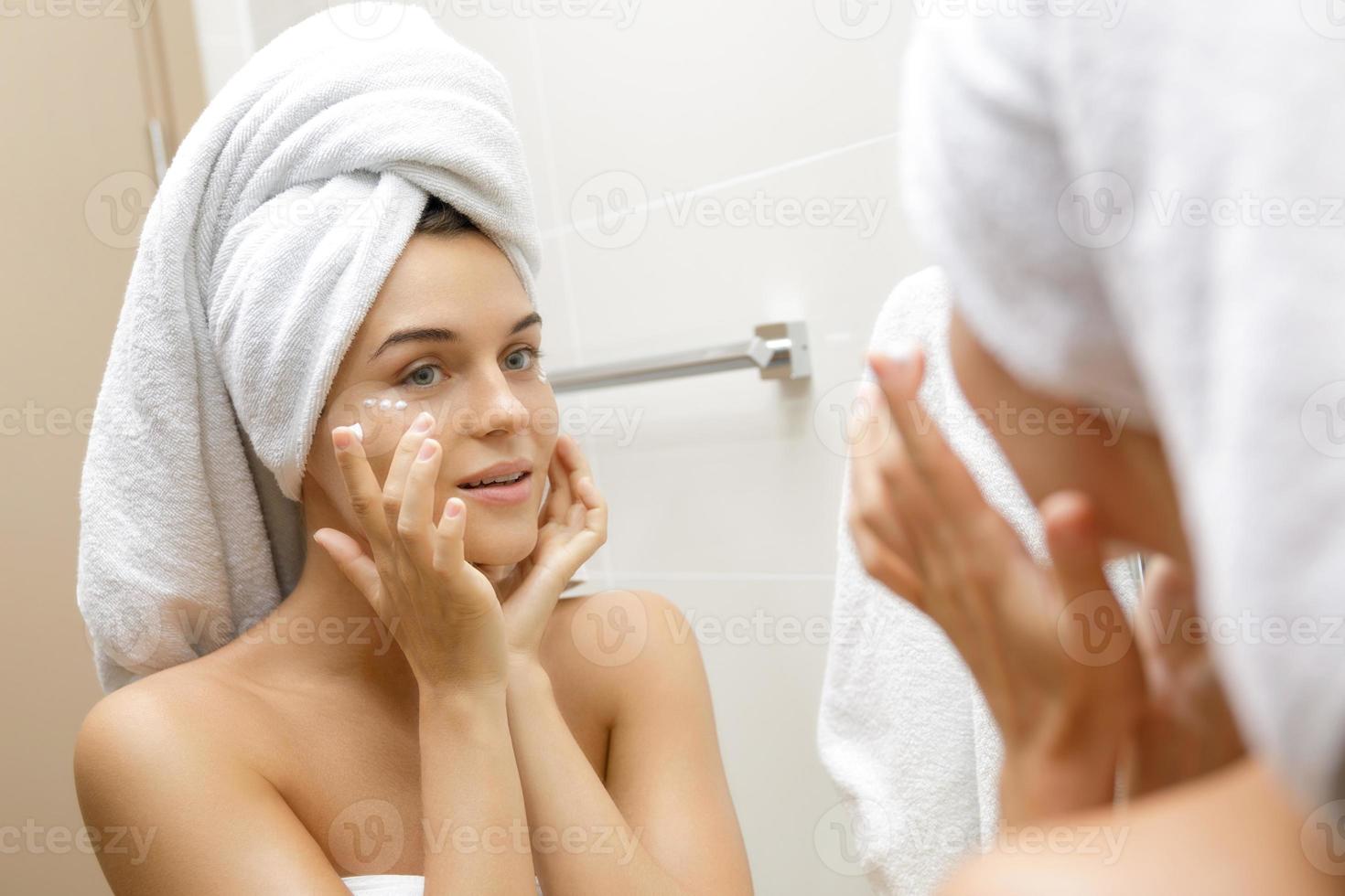 Woman using moisturizing and anti-aging cream under her eyes photo