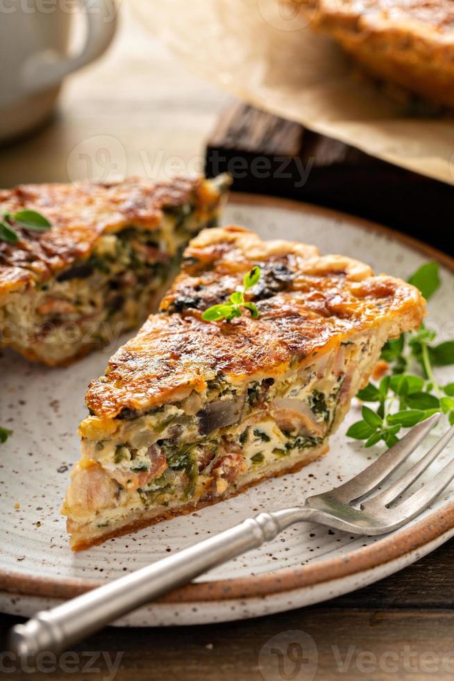 Bacon, mushroom and spinach quiche with cheese and herbs photo