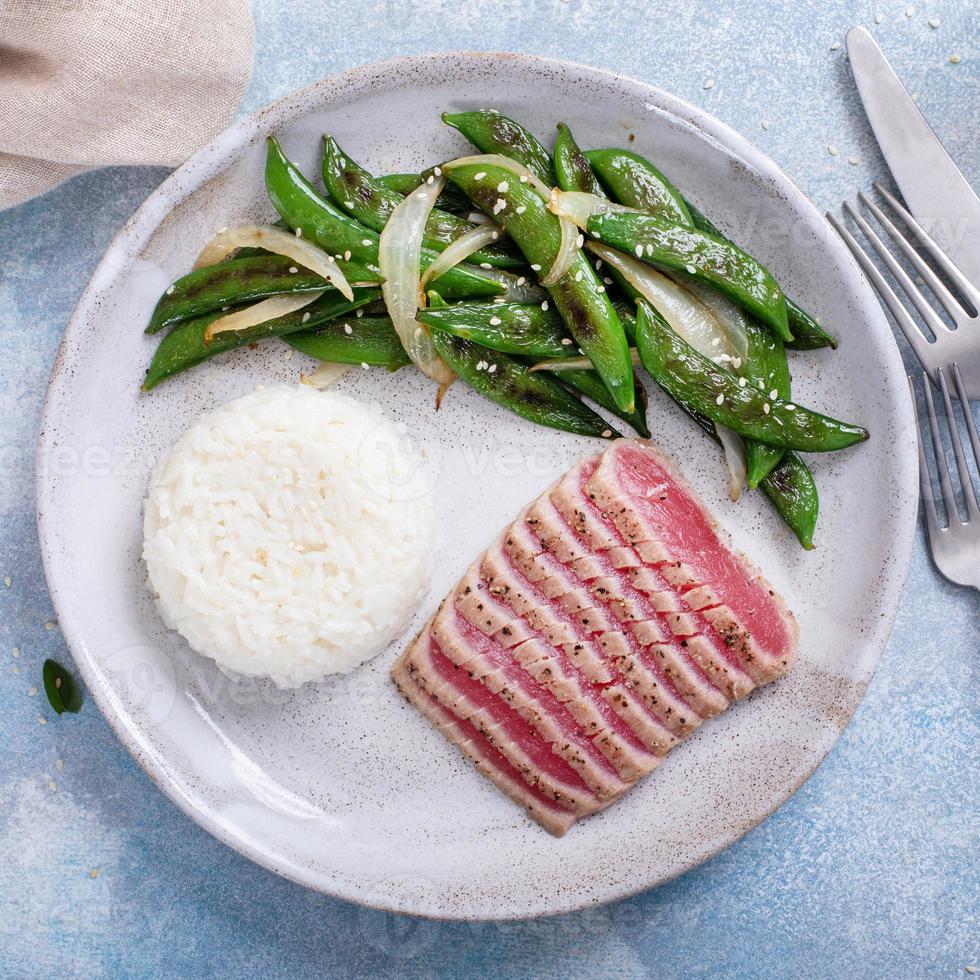 Seared tuna steak with white rice and green peas photo