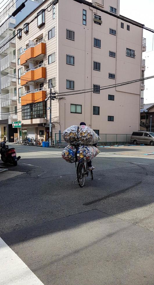 An unidentified person on a street in Osaka is riding a bicycle with a pile of used cans photo