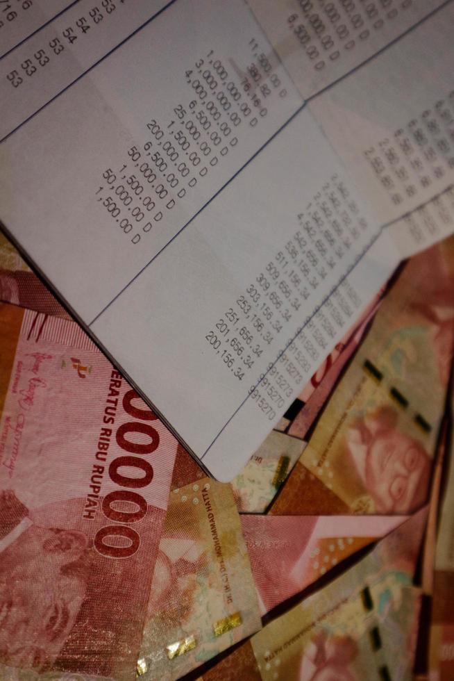 A savings book on top of several hundred thousand rupiah bills scattered around. photo