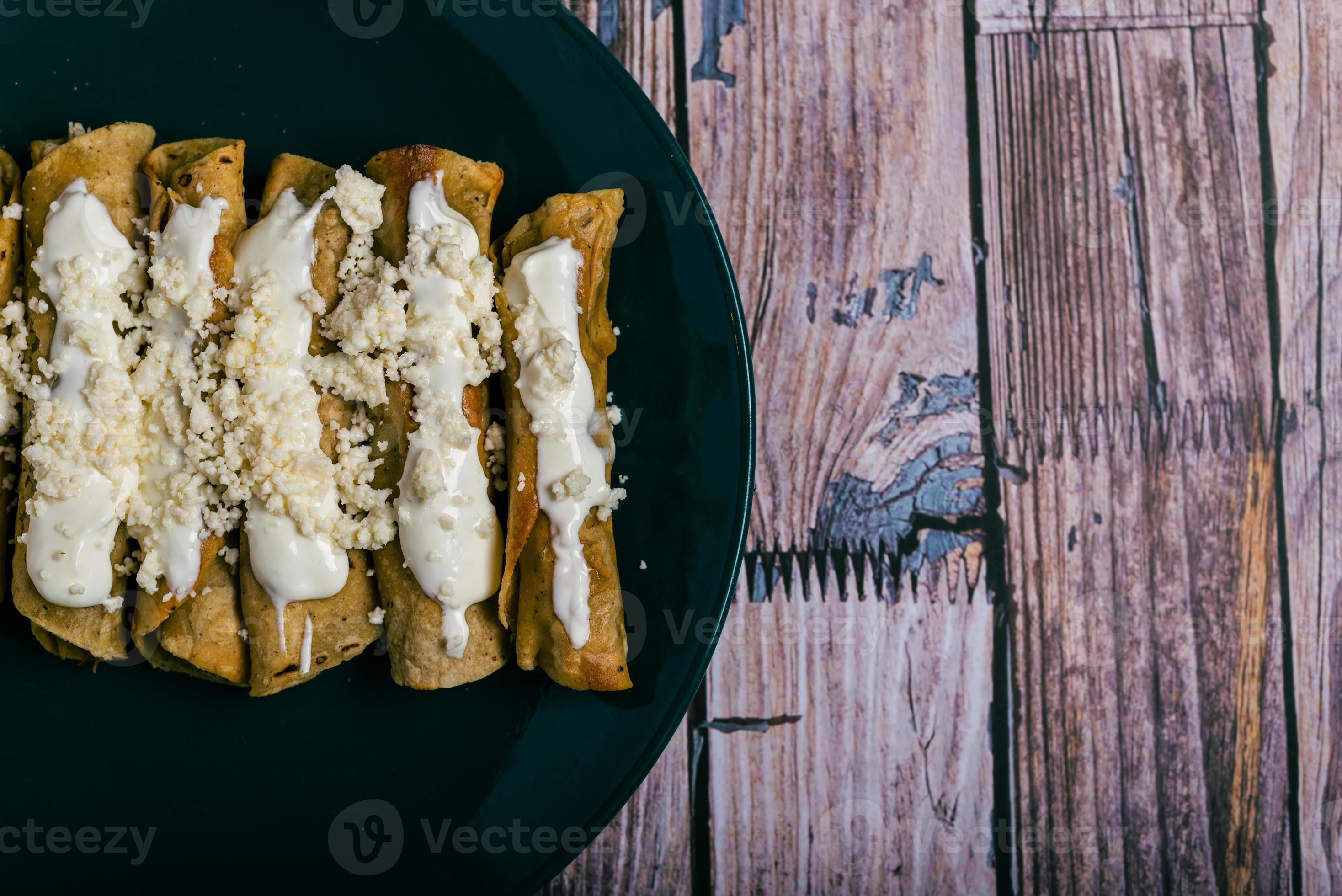 tacos flauta con queso y crema sobre una mesa de madera. antojitos