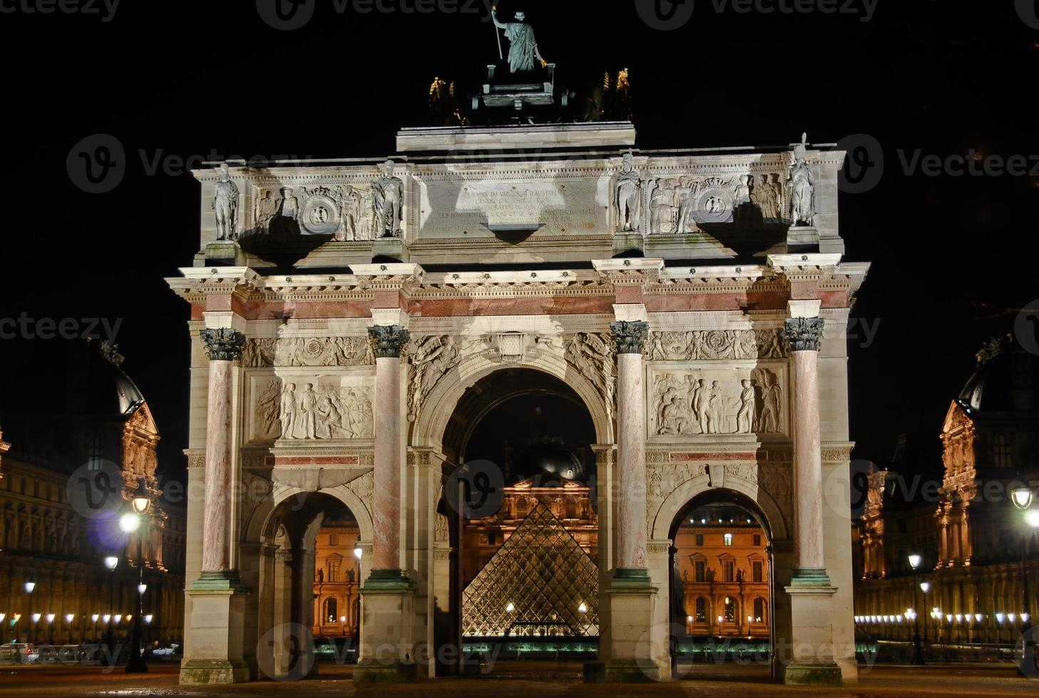 Arc de Triomphe du Carrousel against the background of the Louvre Museum in Paris, France at night. photo