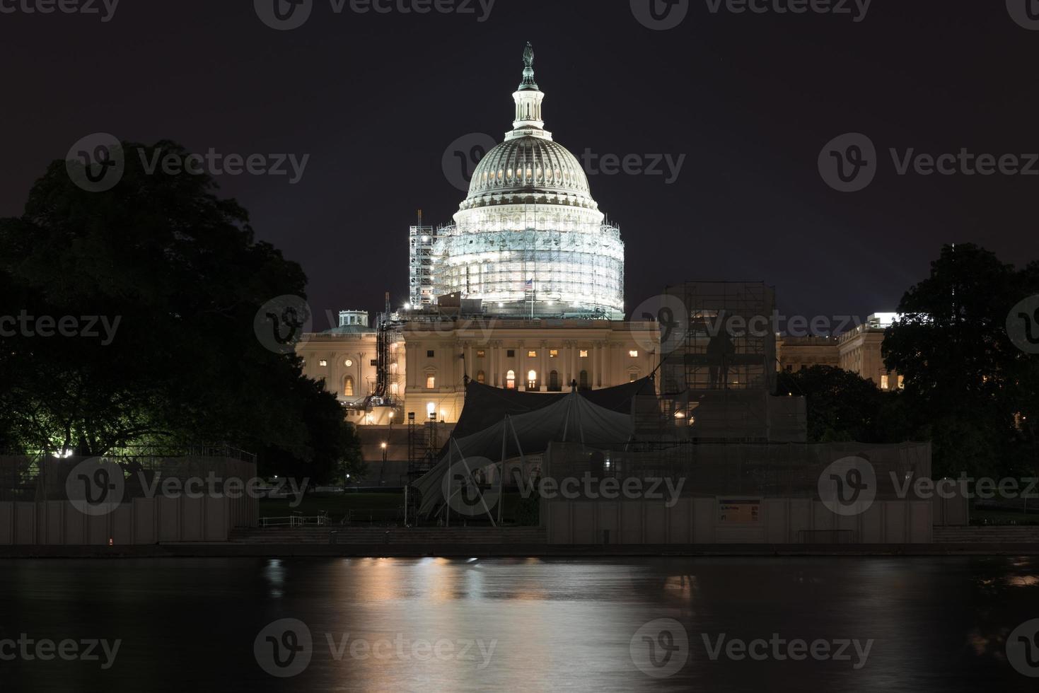The US Capitol Building under scaffolding as seen across the reflecting pool at night in Washington, DC. photo