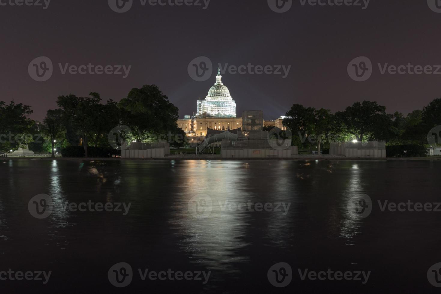 The US Capitol Building under scaffolding as seen across the reflecting pool at night in Washington, DC. photo