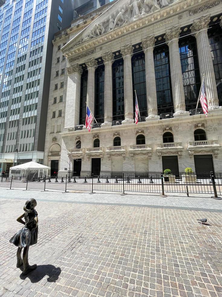 New York City - April 18, 2021 -  Fearless Girl Statue looking up at New York Stock Exchange building at Wall Street in Manhattan, New York City, USA. photo