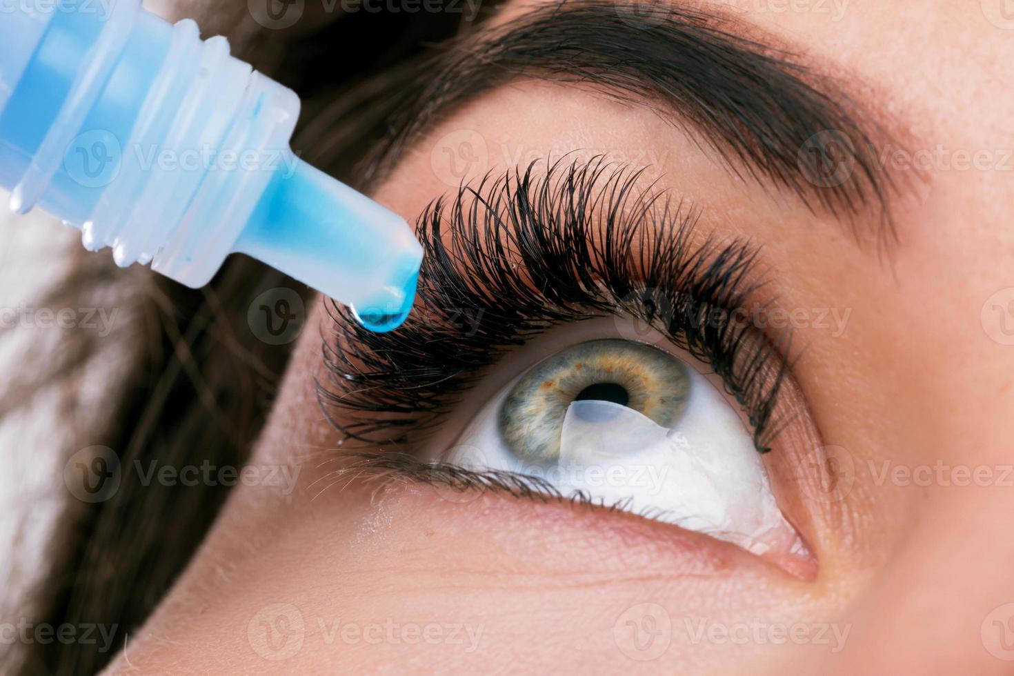 Studio shot of beautiful woman using eye drops photo