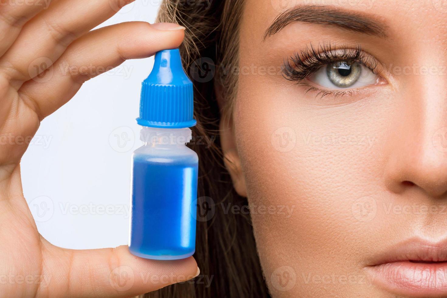 Studio shot of beautiful woman using eye drops photo