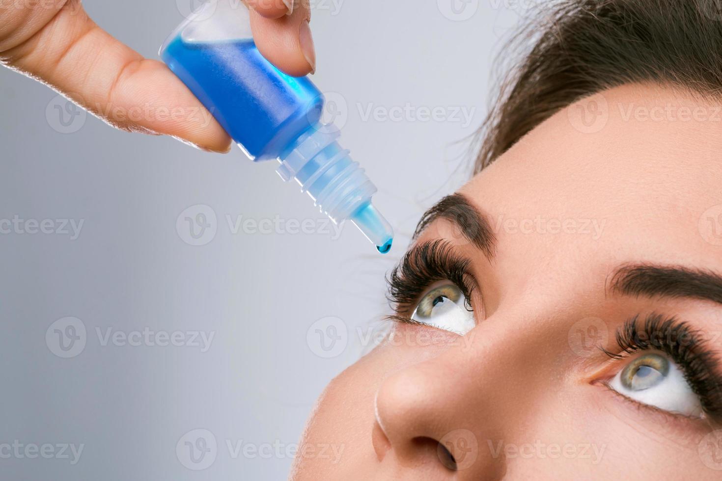 Studio shot of beautiful woman using eye drops photo